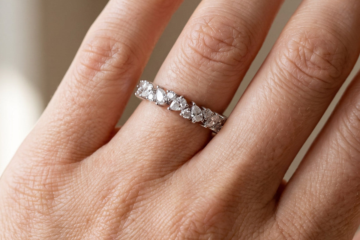 Hand wearing a slim lab grown diamond band set with pear and round stones, close up in soft daylight, Draco Diamond