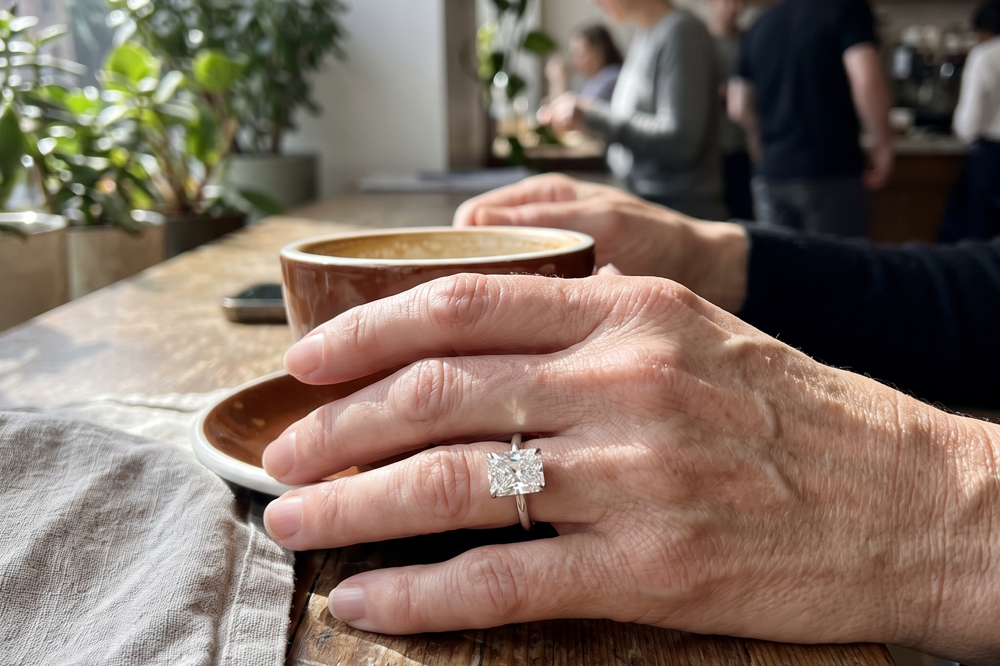 Large radiant cut lab diamond solitaire ring worn on a hand at a cafe table showing true scale, Draco Diamond