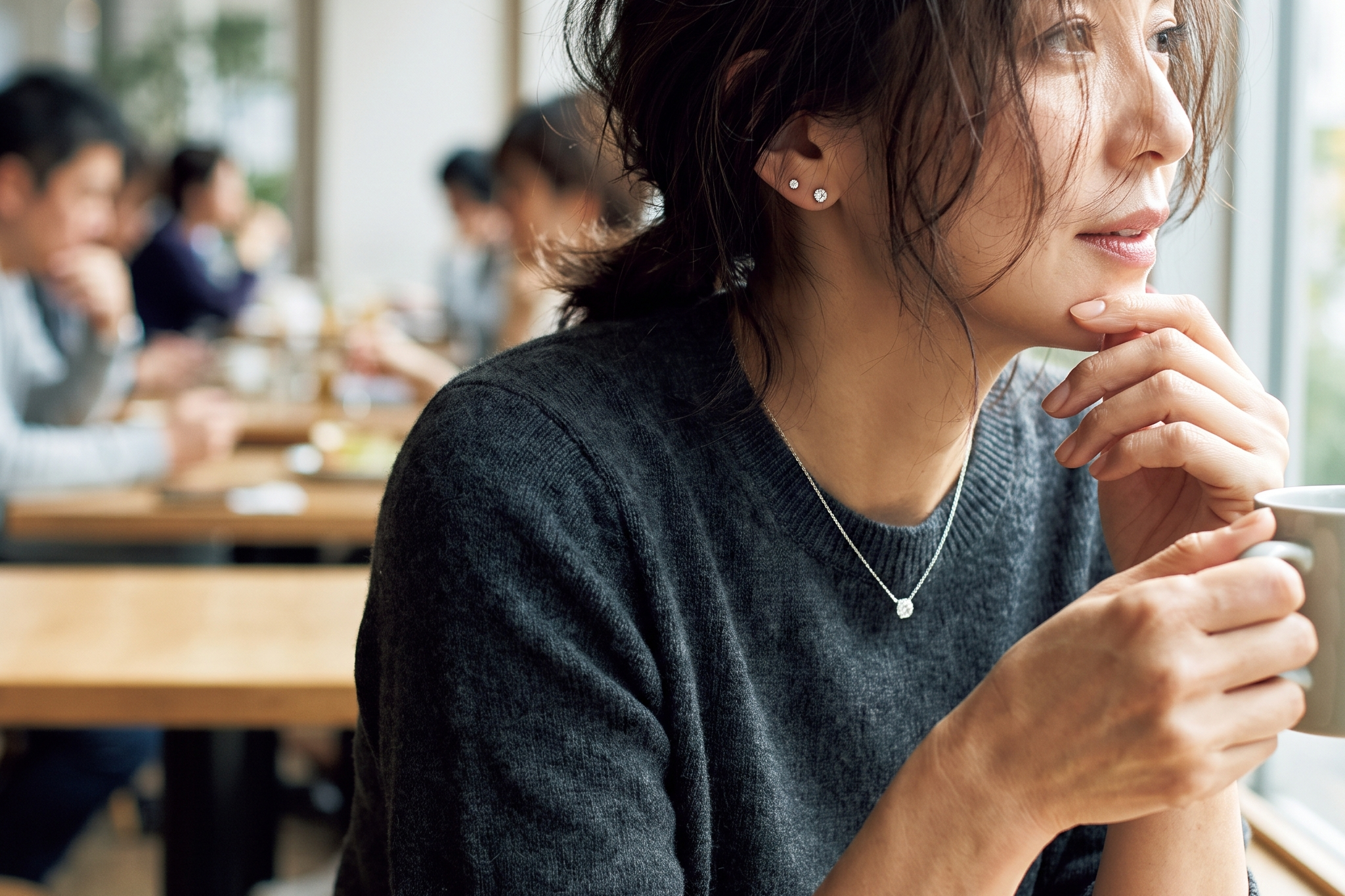 Woman wearing lab diamond stud earrings and a fine pendant in an everyday cafe setting, Draco Diamond