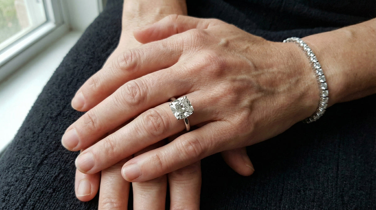 Two hands resting together in window light wearing a lab grown diamond tennis bracelet and a solitaire ring in white metal, showing how metal colour reads against skin, Draco Diamond