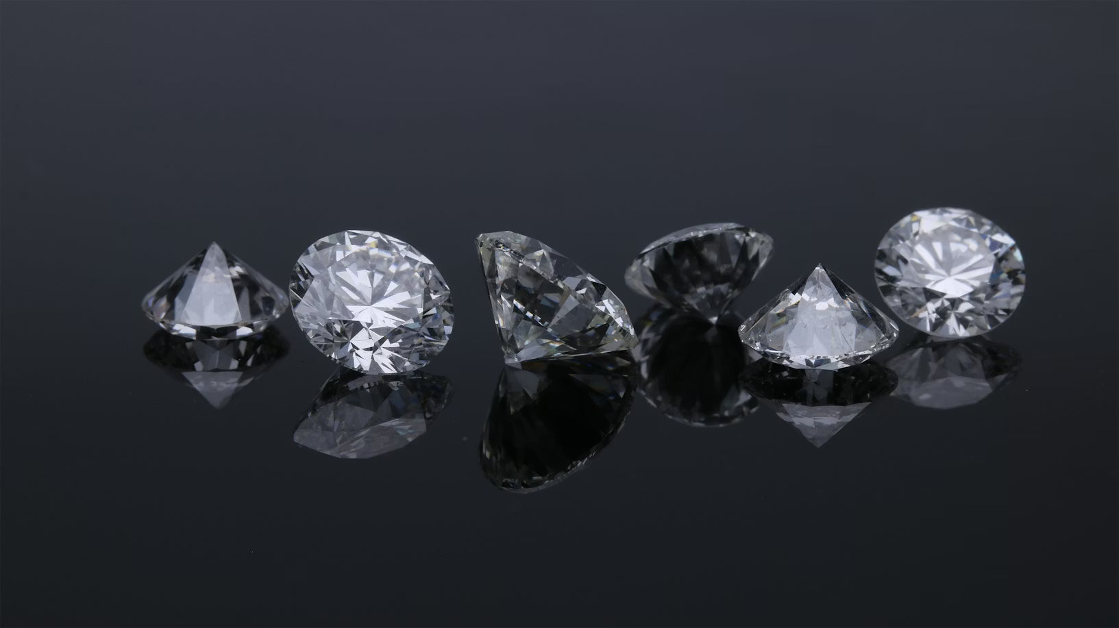 Six loose round brilliant lab grown diamonds on a dark reflective surface, Draco Diamond