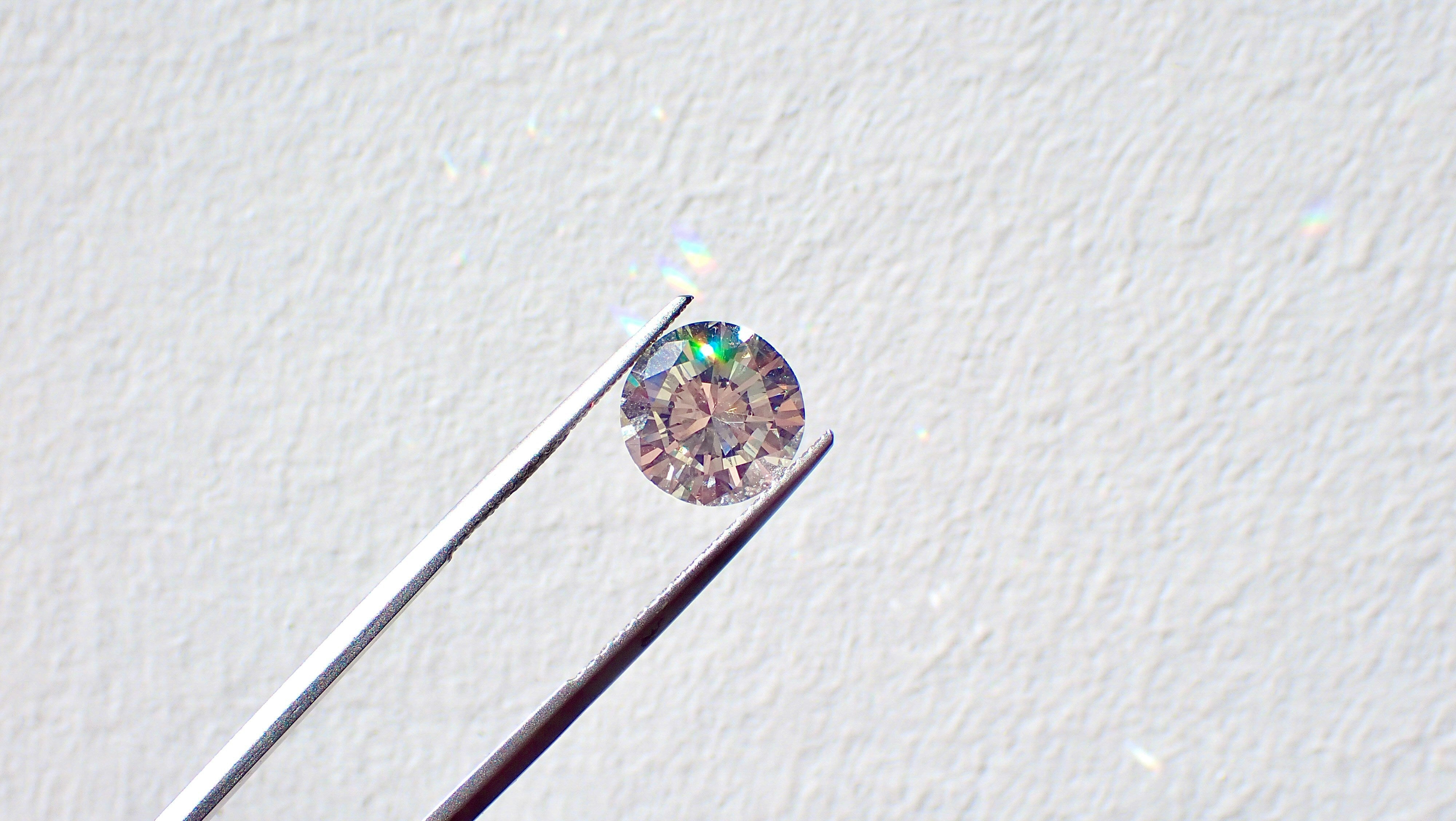 Round brilliant stone held in tweezers throwing colored fire, lab grown diamond versus moissanite, Draco Diamond