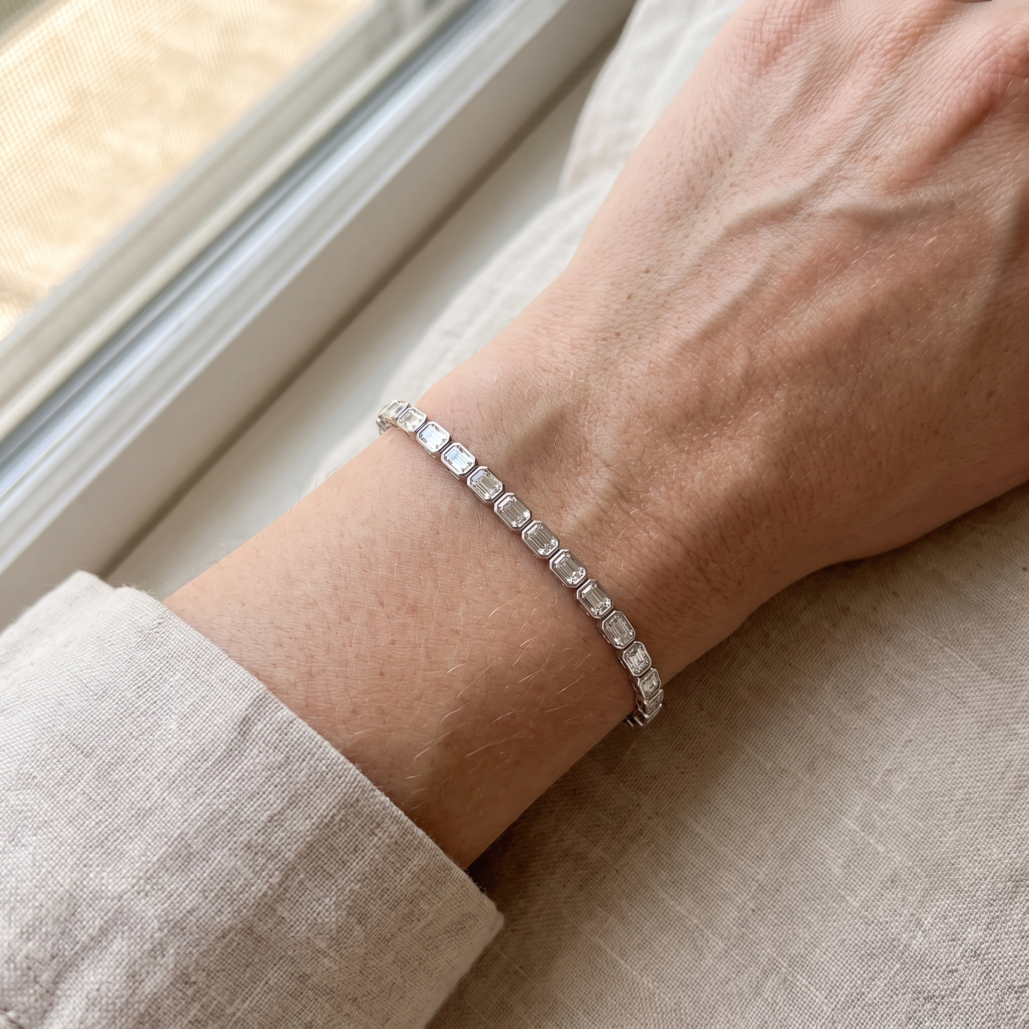 9ct emerald cut lab grown diamond tennis bracelet worn on wrist resting on linen, candid editorial