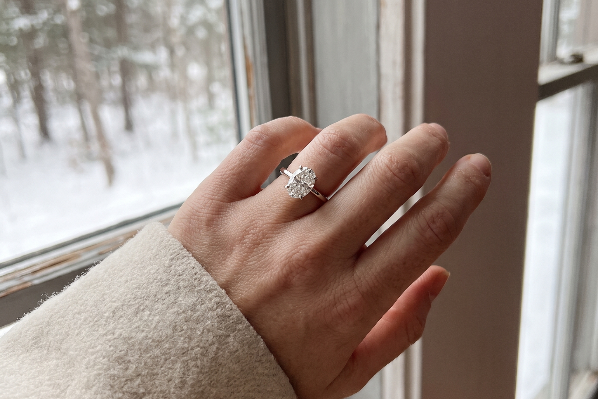 Oval lab grown diamond solitaire engagement ring worn on the hand by a snowy window in Canada, IGI certified, Draco Diamond
