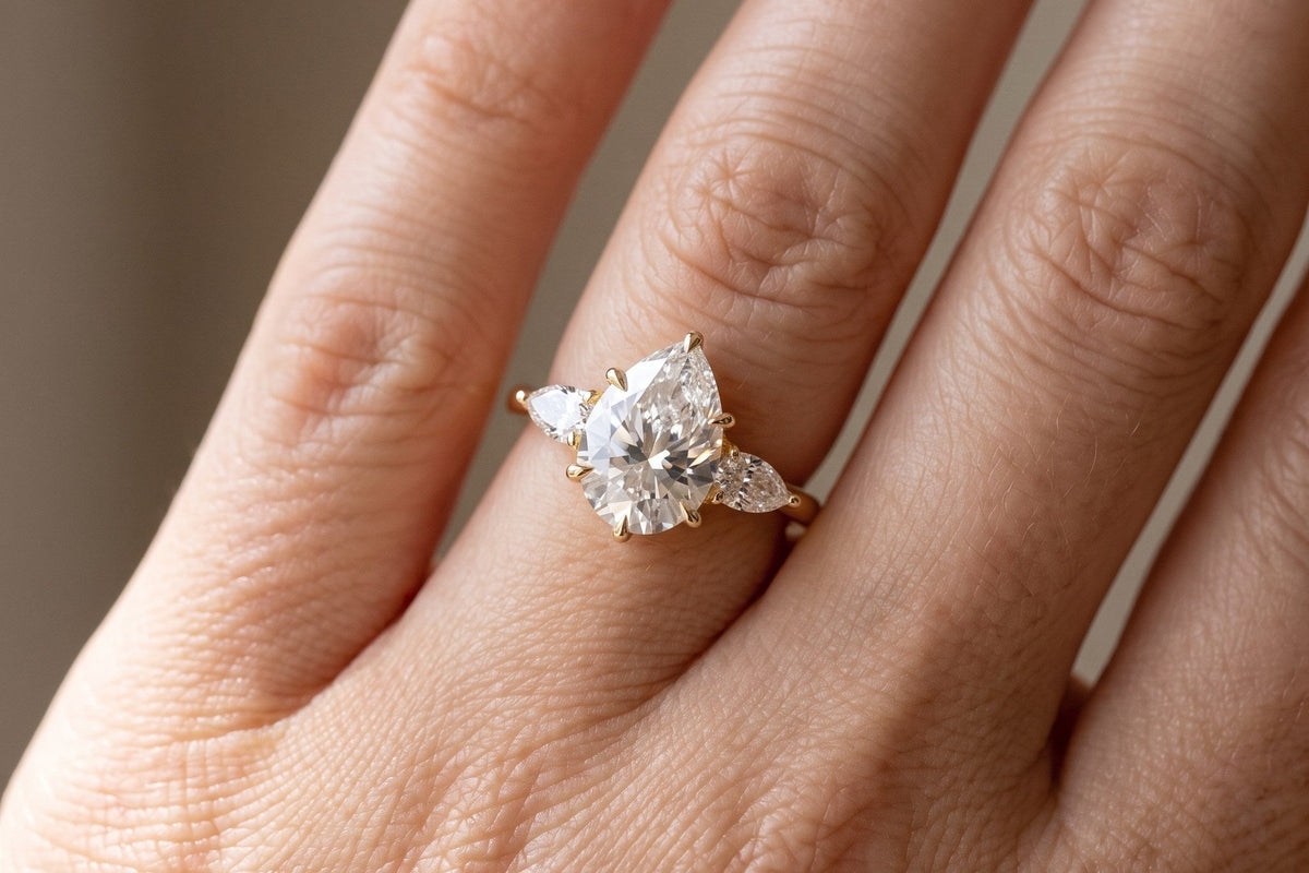 Hand wearing a pear three stone lab grown diamond engagement ring in yellow gold, close up in daylight, Draco Diamond