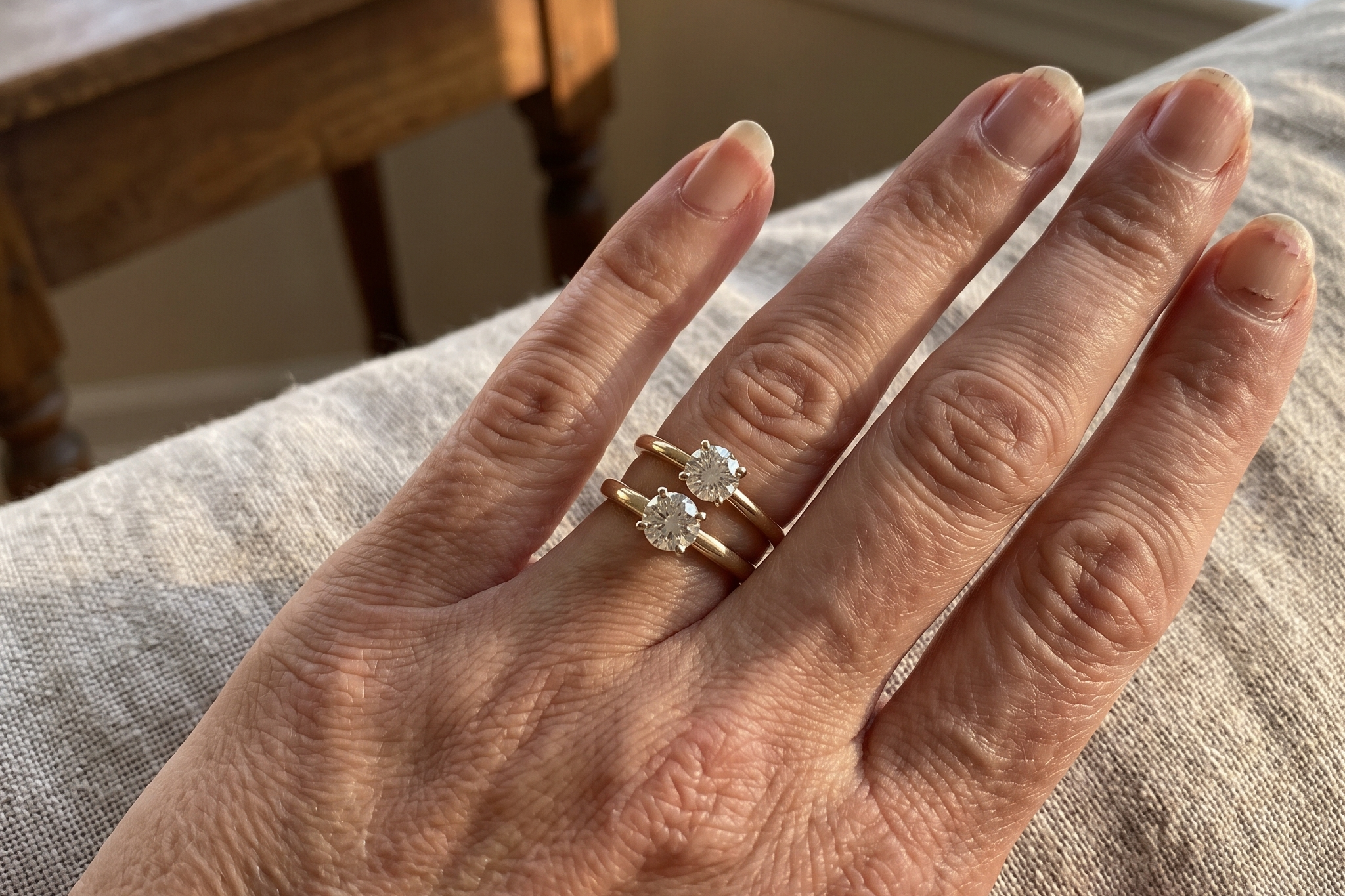 Two round solitaire lab grown diamond engagement rings worn side by side on a hand in warm daylight, one carat versus one and a half carat size difference, Draco Diamond