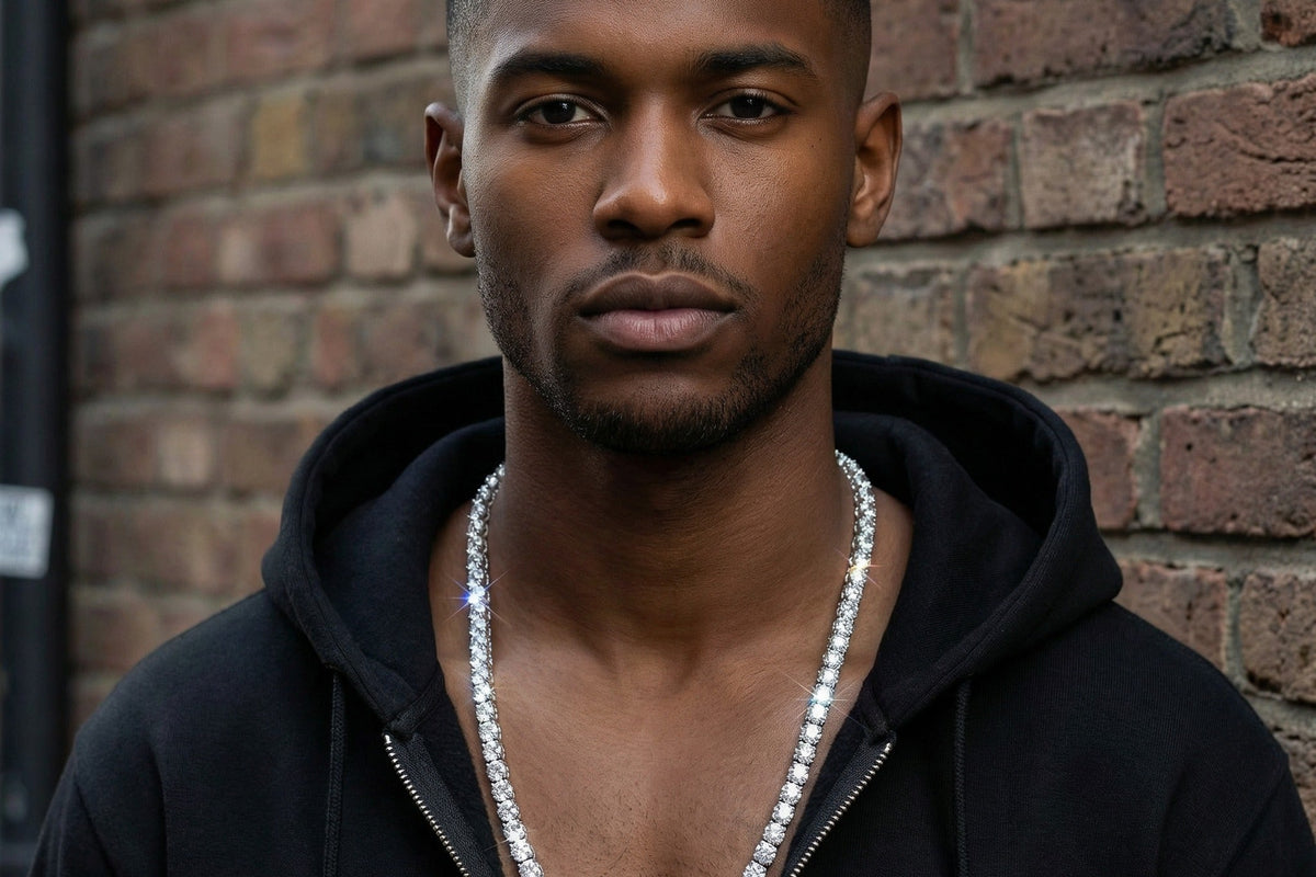 Man wearing a lab grown diamond tennis chain over a dark hoodie against a brick wall in daylight, showing chain width at true worn scale, Draco Diamond