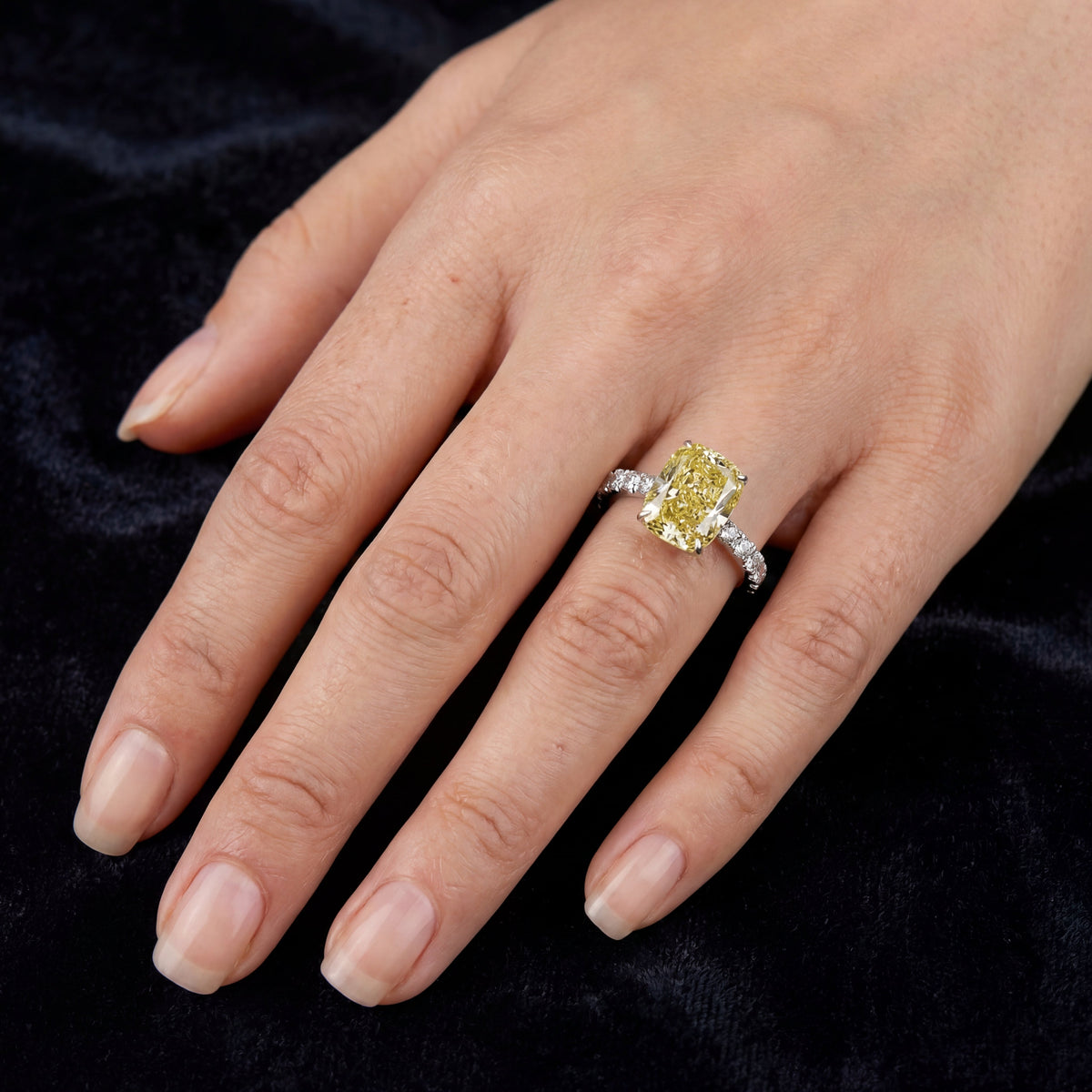 4.59ct fancy vivid yellow cushion lab grown diamond ring worn on a hand on dark velvet