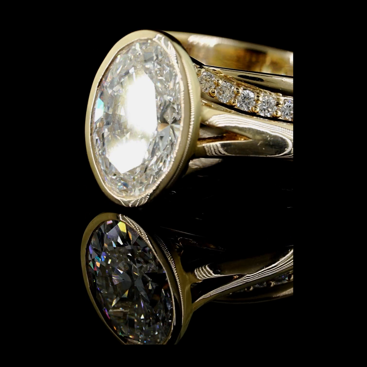 3ct oval bezel lab grown diamond bridal set, 14k yellow gold, real video still on black, bezel and pave shoulder close up