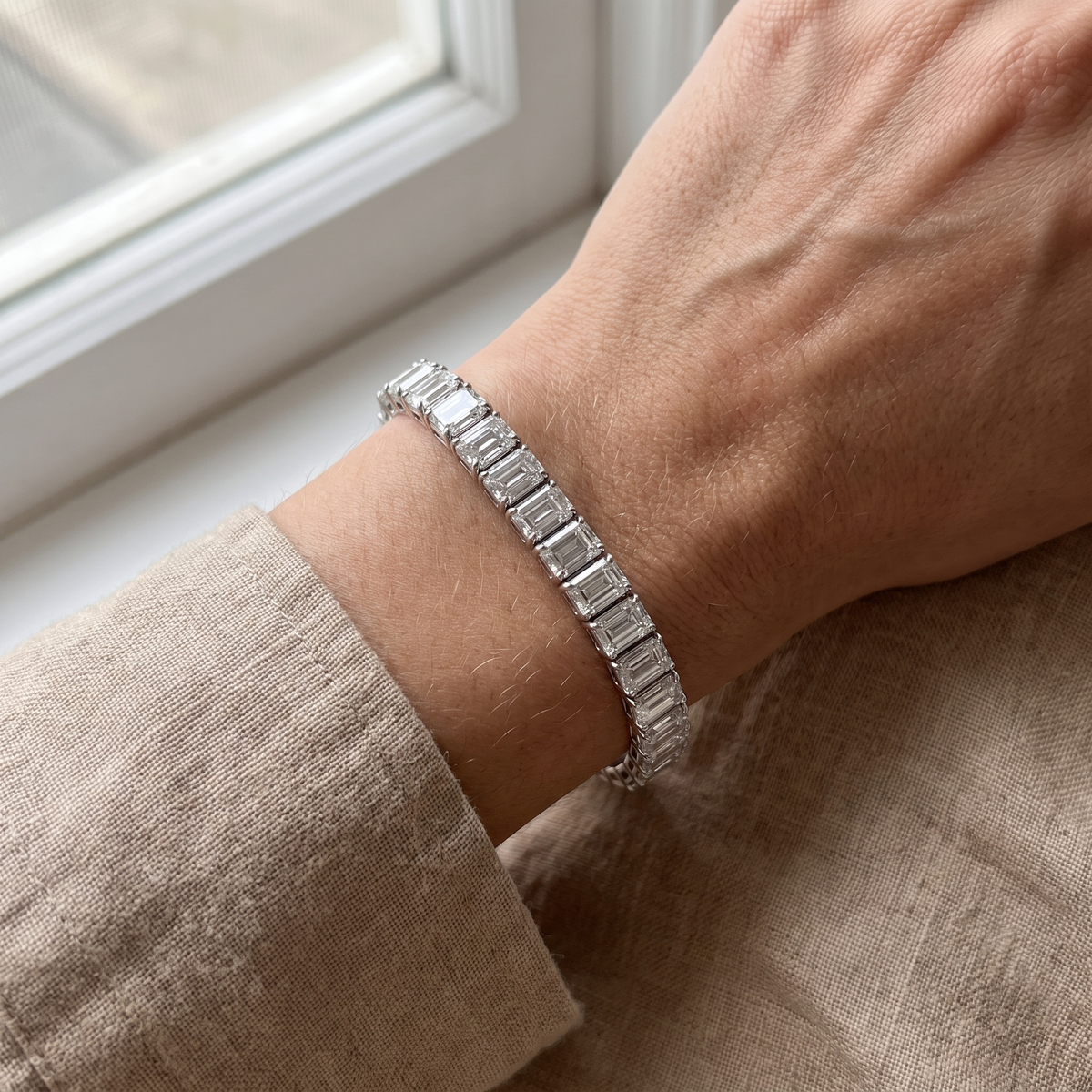 31.87ct emerald cut lab grown diamond tennis bracelet worn on wrist resting on linen, candid editorial