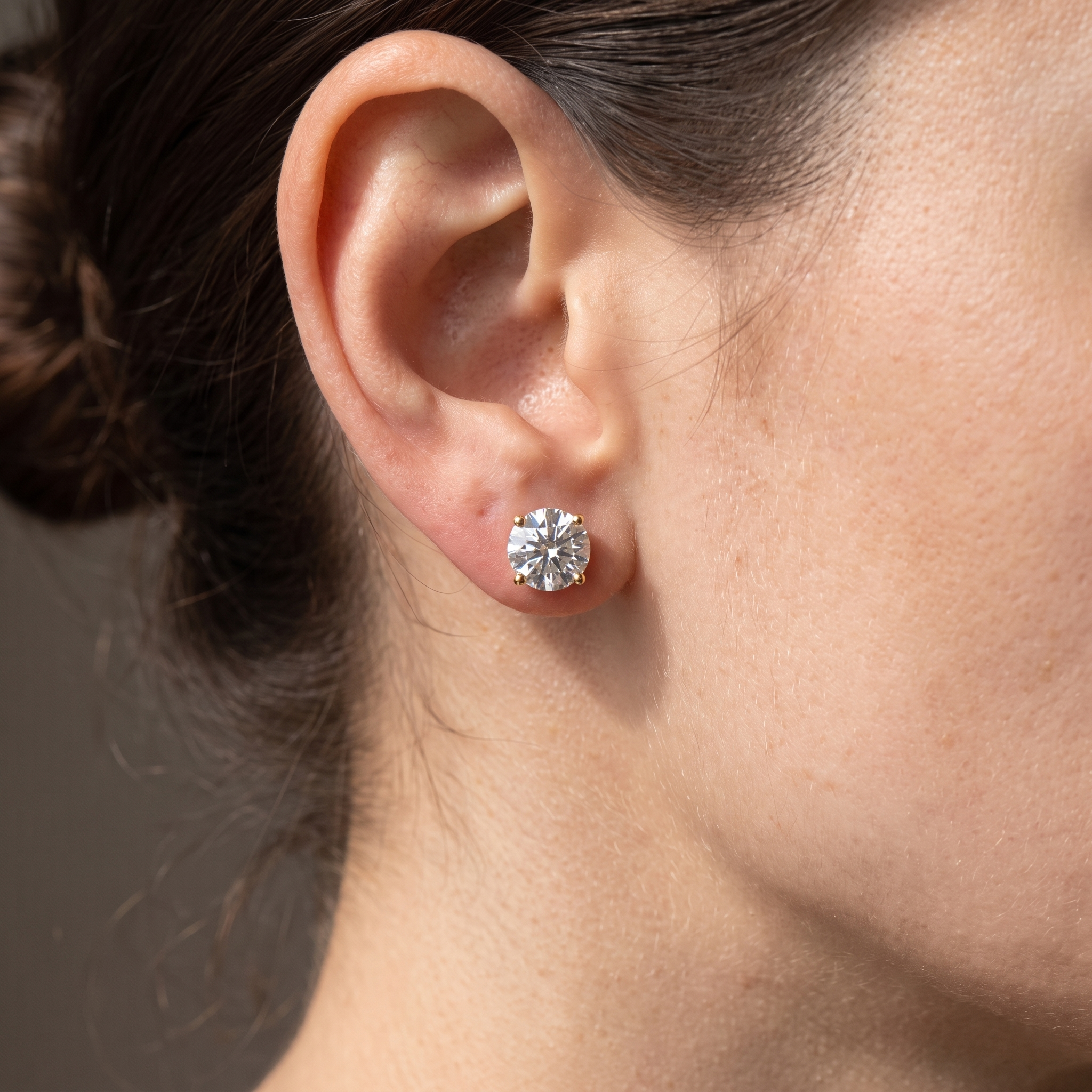 2 carat round lab grown diamond stud earring worn on the ear, 8.1mm stone in a yellow gold four-prong basket