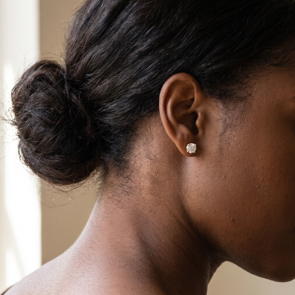 2 carat round lab grown diamond stud earring worn on the ear, viewed from behind with hair swept up, yellow gold four-prong basket